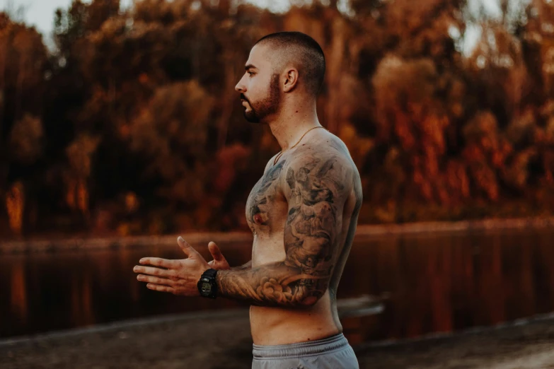 a tattooed man in shorts standing in front of a lake