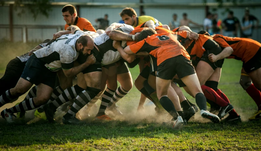 a rugby player in an orange jersey is trying to get through a pile of players in a game