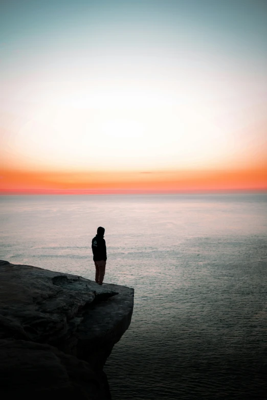 a man standing at the edge of a cliff looking out at the ocean