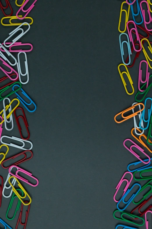 a group of different colored paper clips on top of a black surface