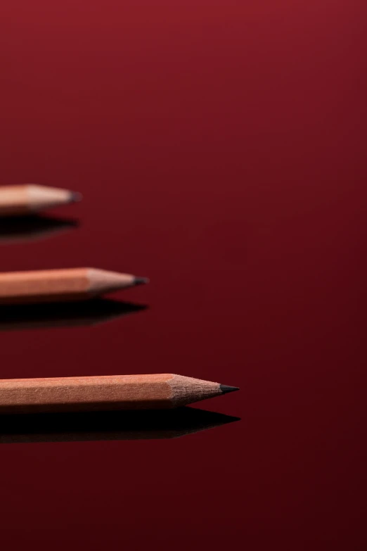 three pencils lie close together on a maroon surface