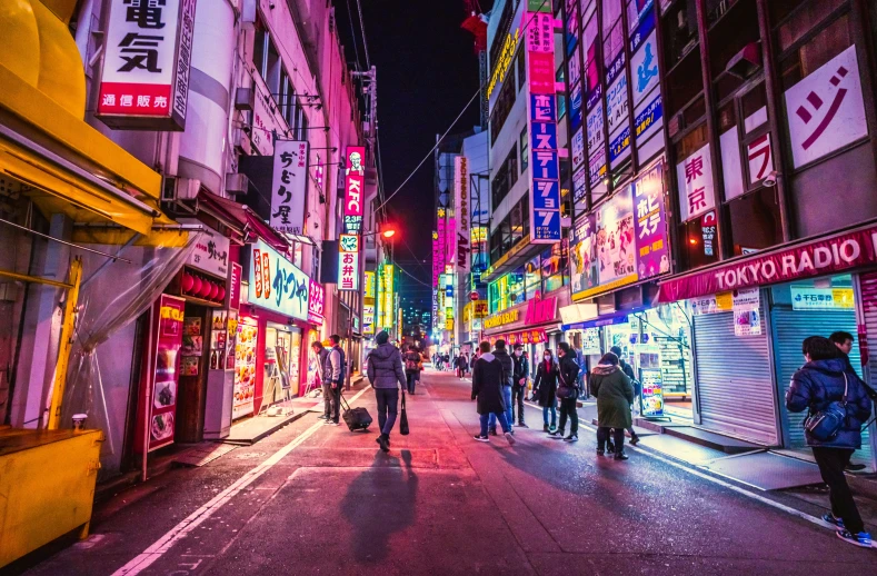 the people are walking down the city street in the neon lights