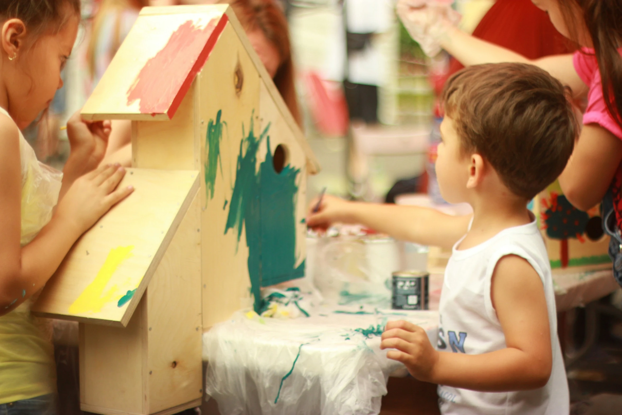 two children standing and playing with a painted birdhouse