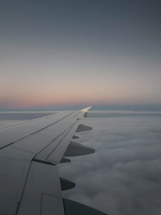 an airplane wing in the air above some clouds