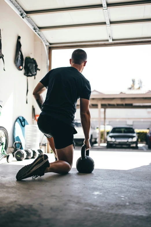 a man squats down and holds a kettle in a garage