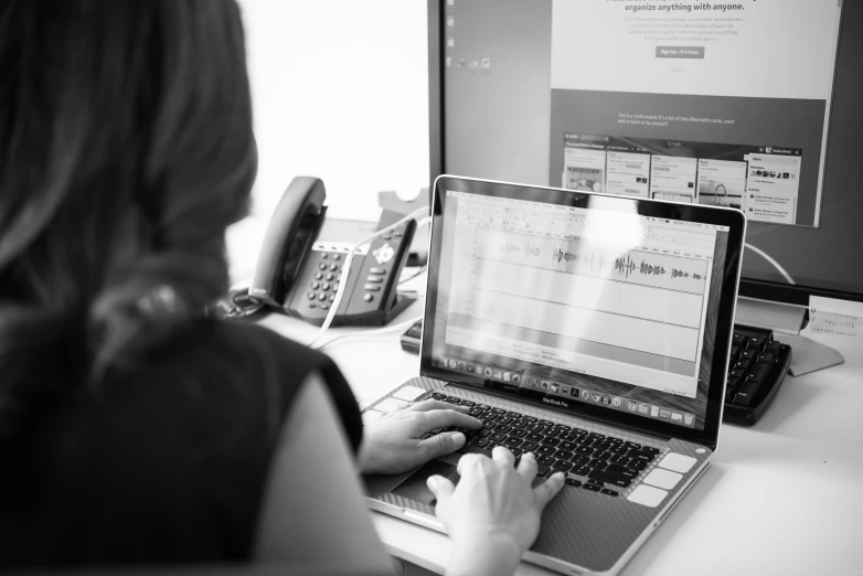 a woman sitting at her computer with a phone near her and a laptop with a web application on her