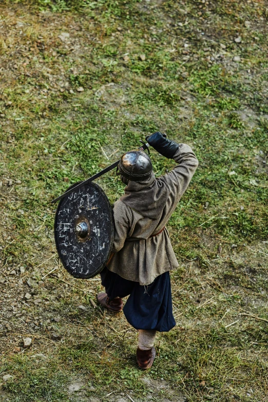 a medieval era figure standing on top of a grass field holding a shield