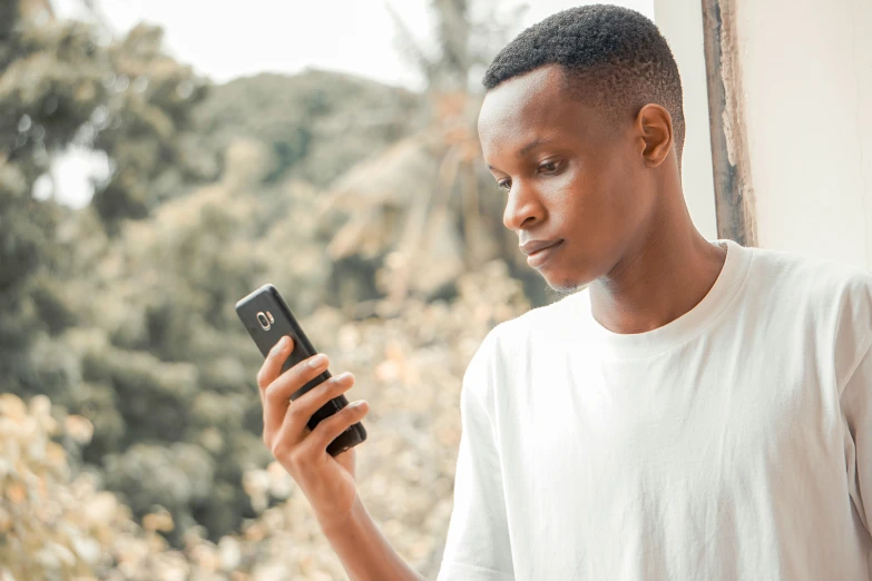 a young man standing next to a window and holding a cellphone