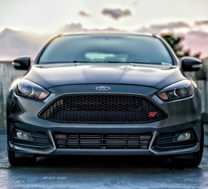 the front end of a black car with clouds in the background