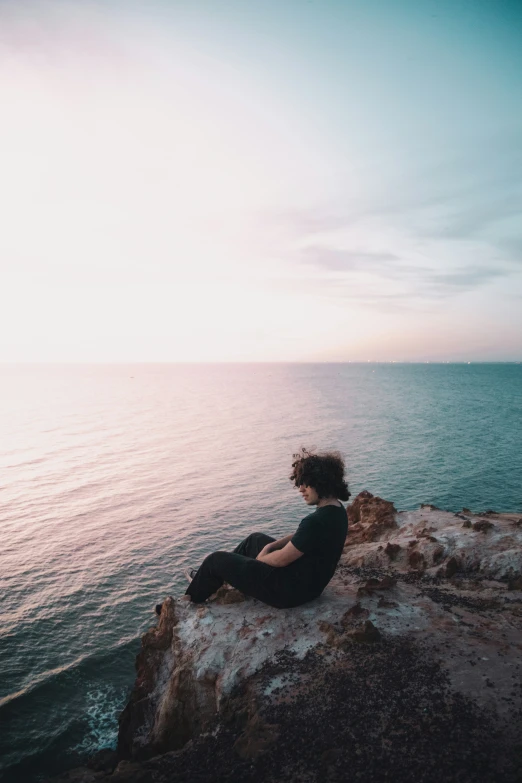 a person is sitting on a rock looking out into the ocean