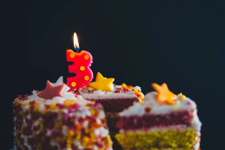 a multi - colored cake with a lit candle sitting on top of it