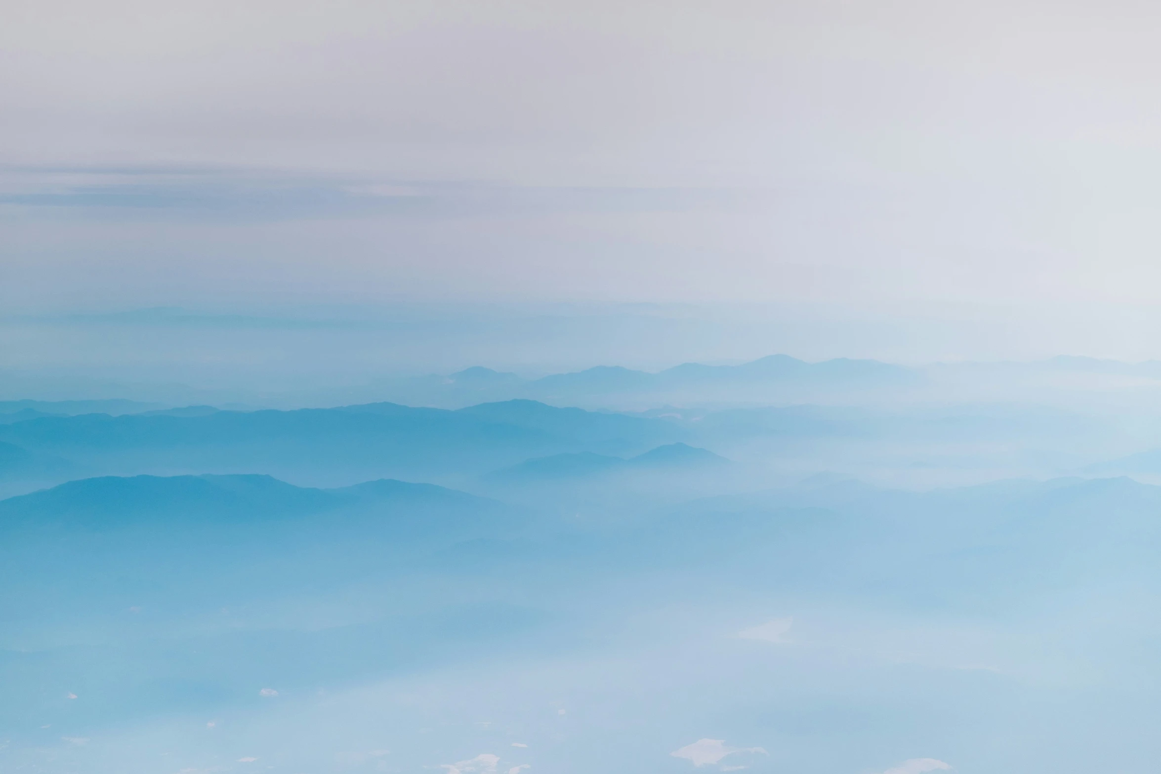 the view out of an airplane window as clouds hover over hills