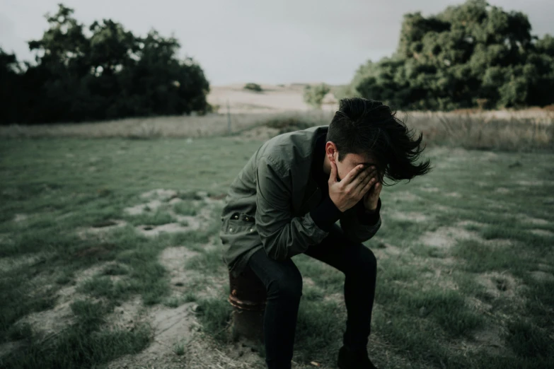 a man with curly hair sitting in a field while covering his face