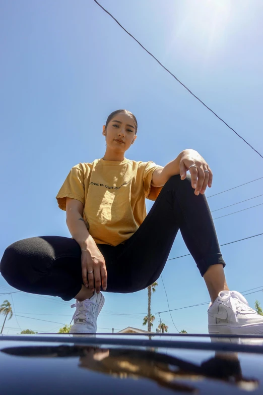 a person wearing black legging sitting on the hood of a car