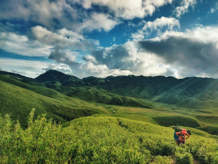 a person with backpacks walking down a grassy hill