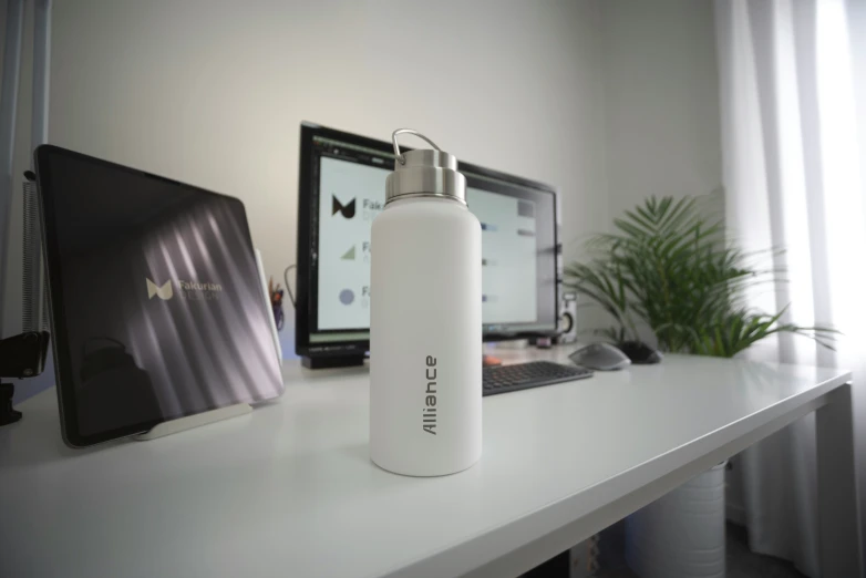 an aluminum water bottle on a white counter in front of a monitor