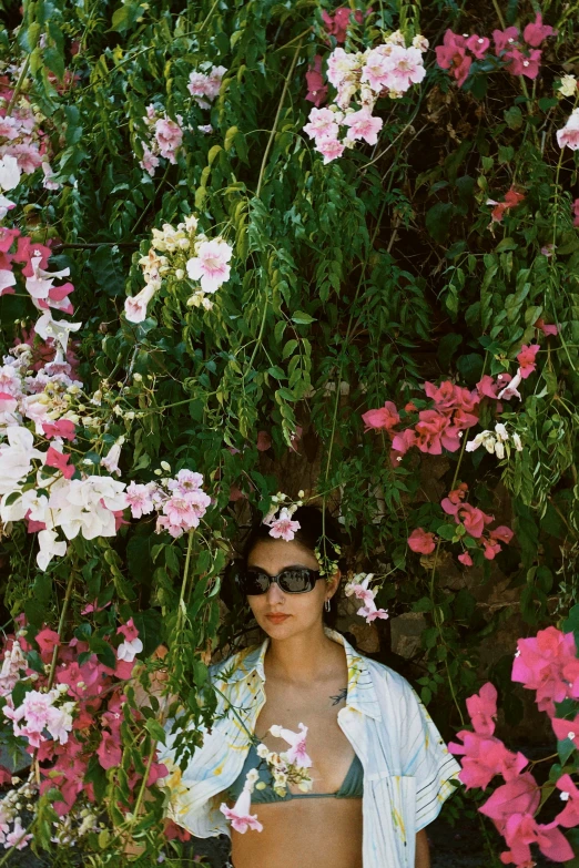 a woman with a jacket and sunglasses is posing in front of pink flowers