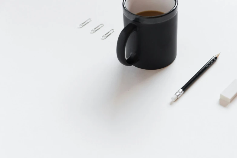 a black coffee mug and pen on a white surface