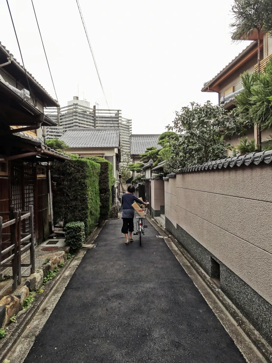 an alley way with an old woman hing a bicycle behind her
