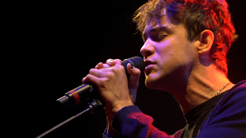 a young man holding a microphone and looking off to the side