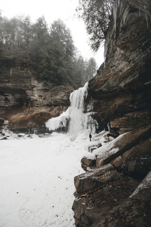 a man standing on a cliff next to a snow covered waterfall