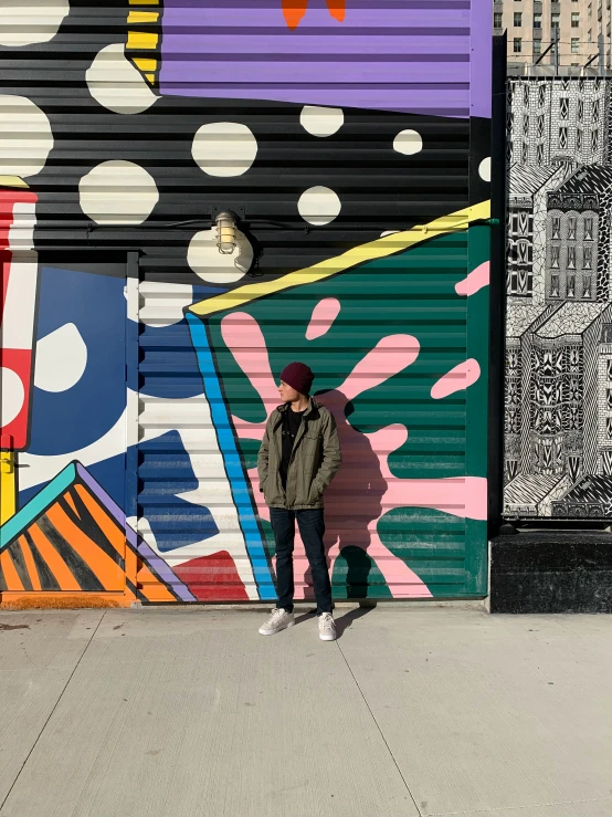 a man standing in front of a colorful mural with black and white dots