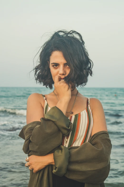 a woman with a scarf around her shoulder is standing in front of the ocean