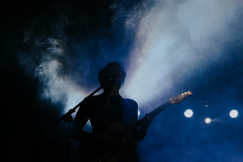 a person holding a guitar while standing under smoke