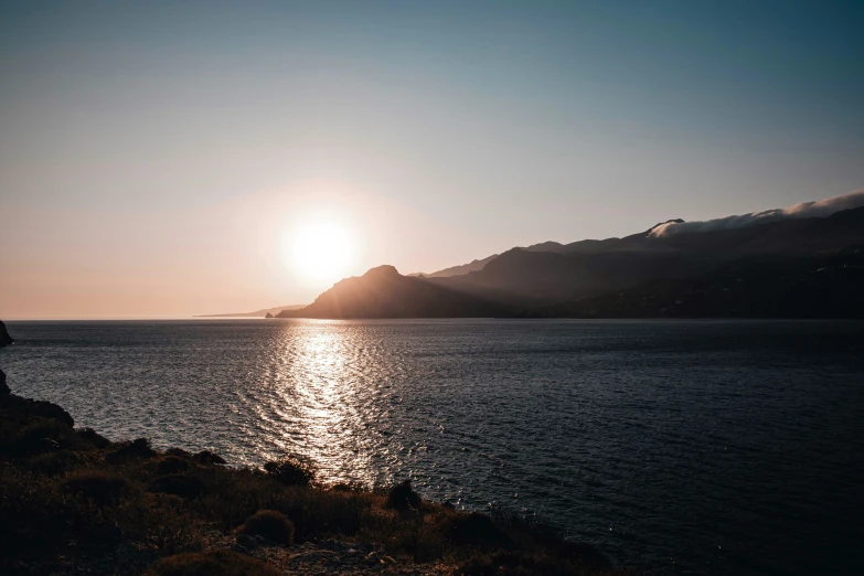 people are sitting at the edge of a cliff on the water, while the sun sets