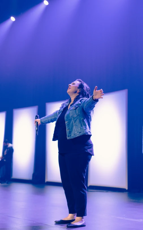 a woman standing on a stage and pointing at some people on the ground