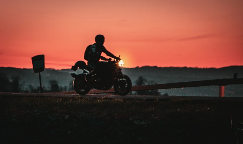 the silhouette of a person on a motorcycle in front of a sunset