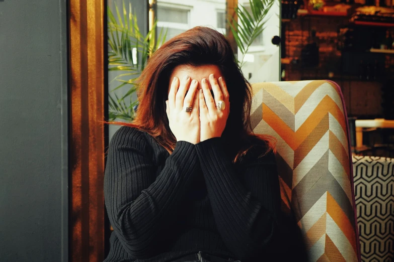 a woman sits in a couch with her hands covering her face