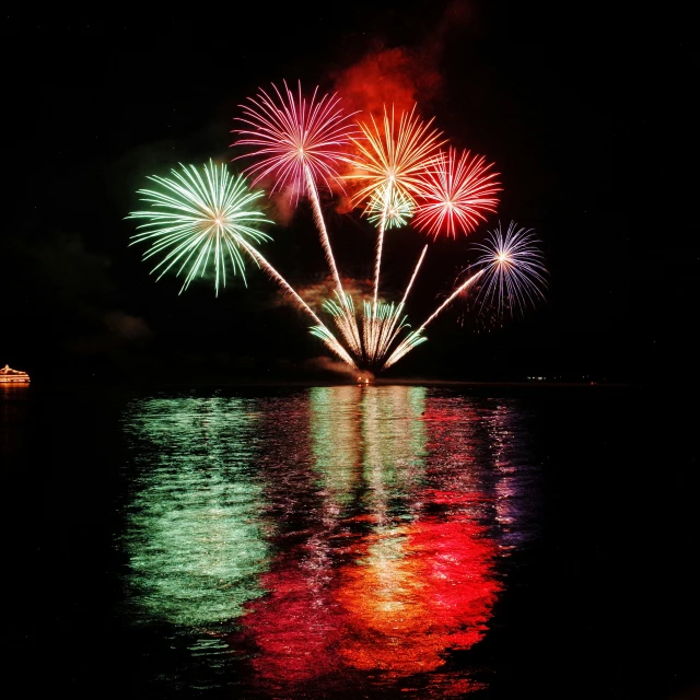 multiple fireworks on a lake reflecting in water