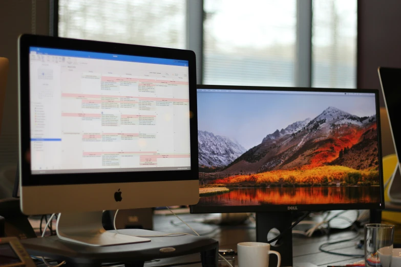 two computers are sitting on the desk side by side