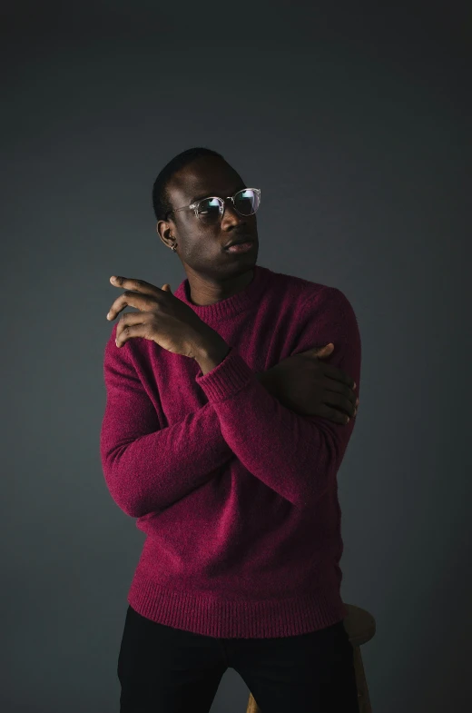 a man in a red sweater is standing with his hands folded over his chest