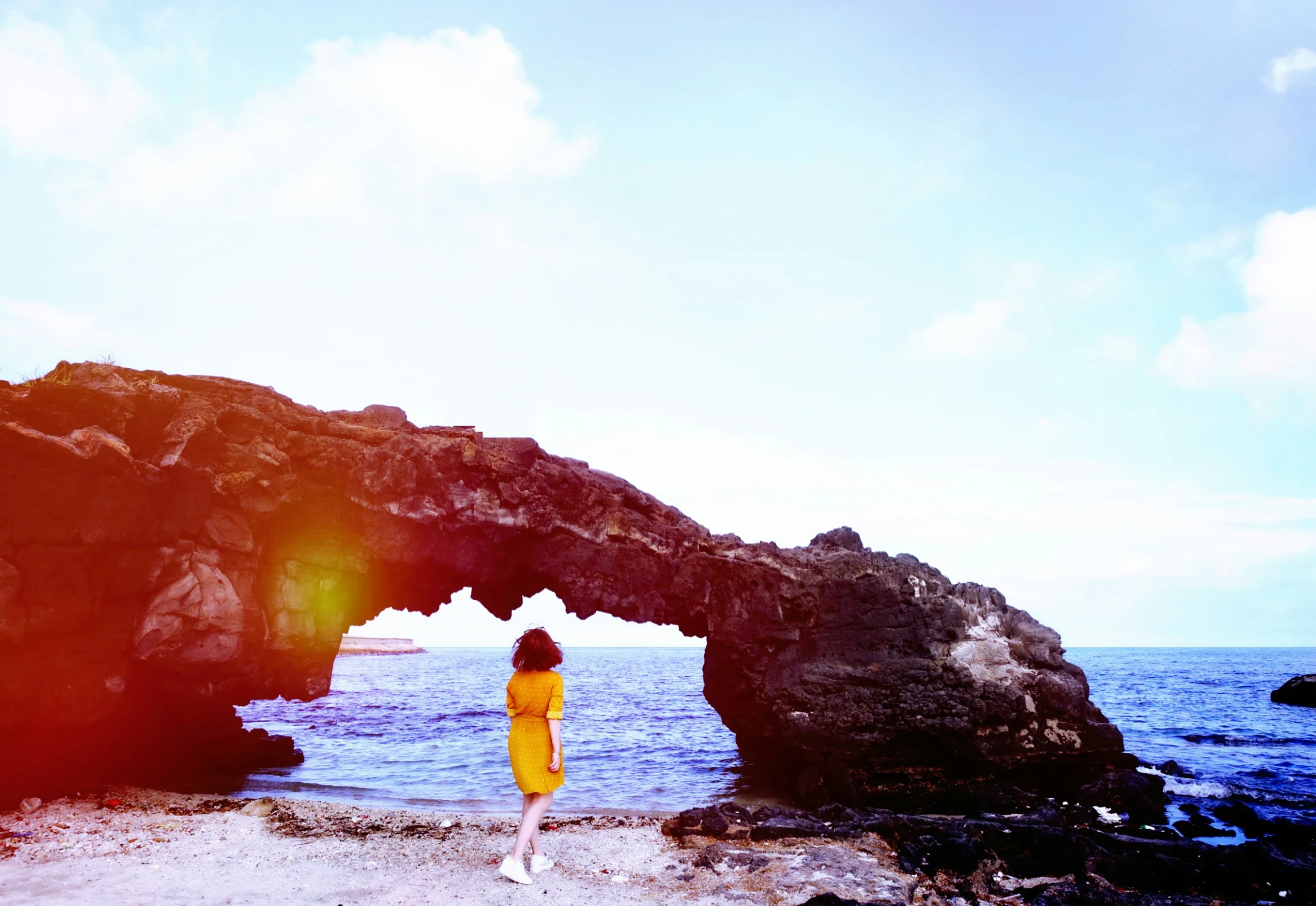 woman standing on the shore near a rocky arch