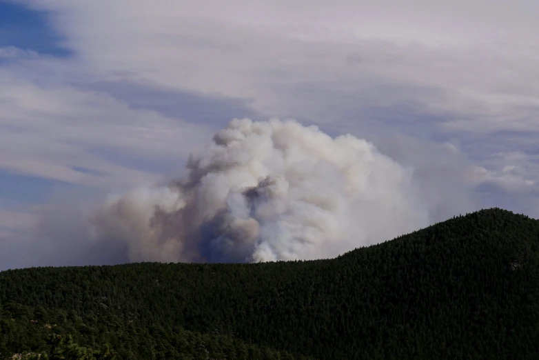 a plume of smoke rises from the top of a hill