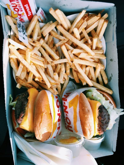 two hamburgers sitting in a box next to fries and ketchup