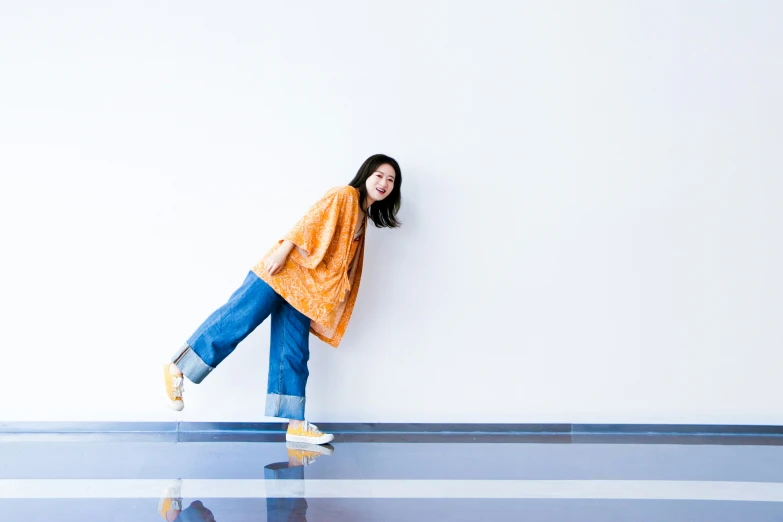 young woman in casual clothing leaning against wall with one leg on the ground