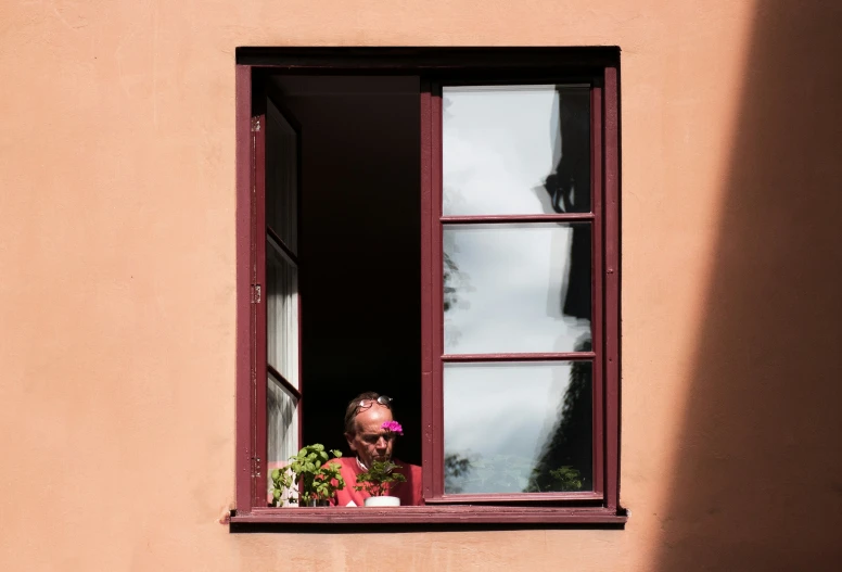 a woman looks out a window and holds flowers in her hand