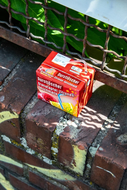 a small box of red jellie sits in front of a fence