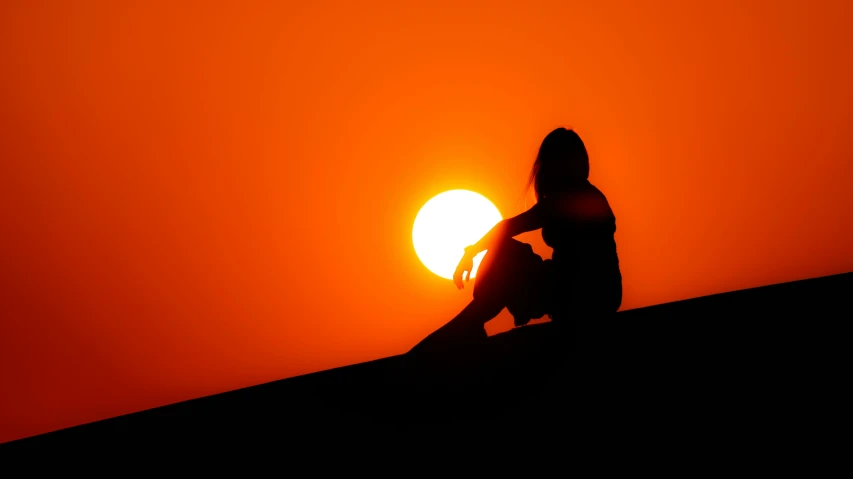 there is a woman sitting on the roof of a building as the sun sets