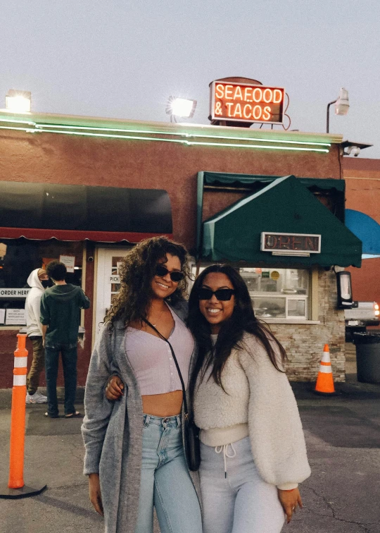 two young women are posing outside of seafood tacos