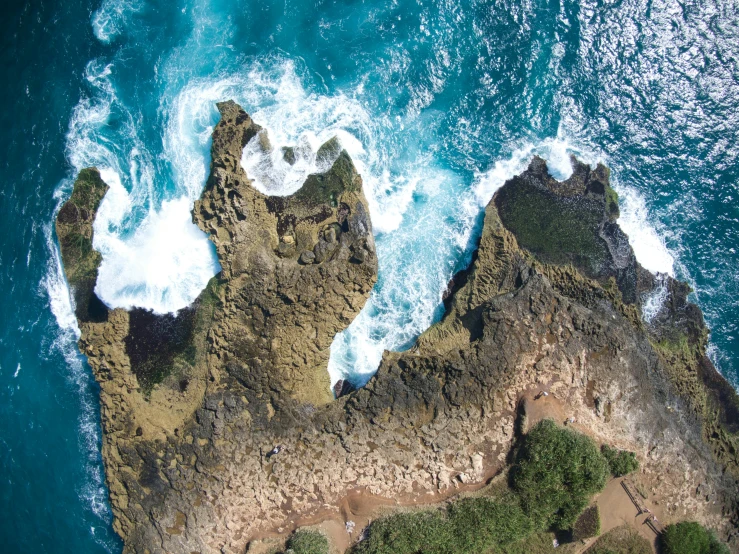 an aerial view of the ocean with two small rocks in the middle of it