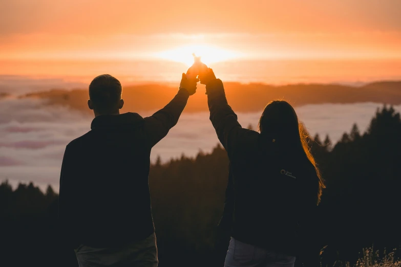 a couple holds hands up in front of the sun