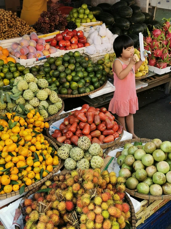 a little girl at an outdoor market selling various fruits