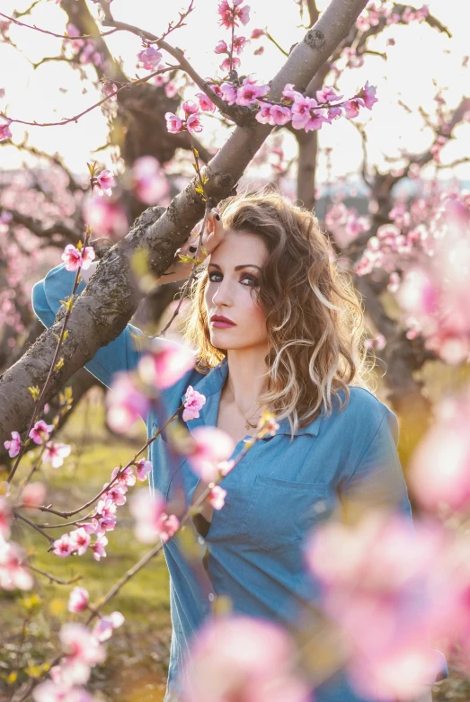 a girl in a blue shirt standing in front of an apple tree with pink blossoms