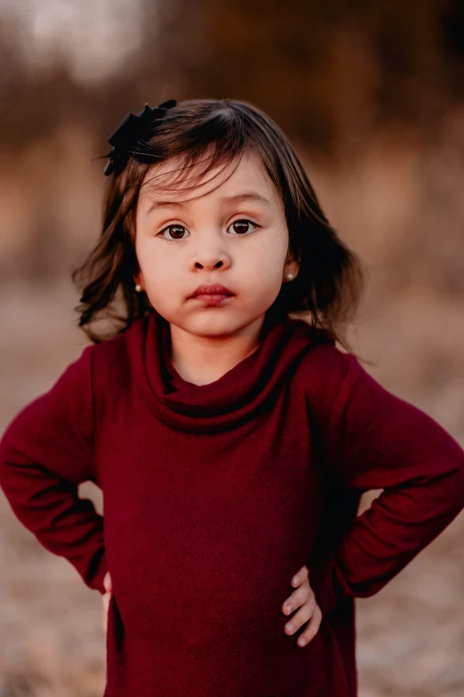 a little girl in a red sweater and a bow is posing