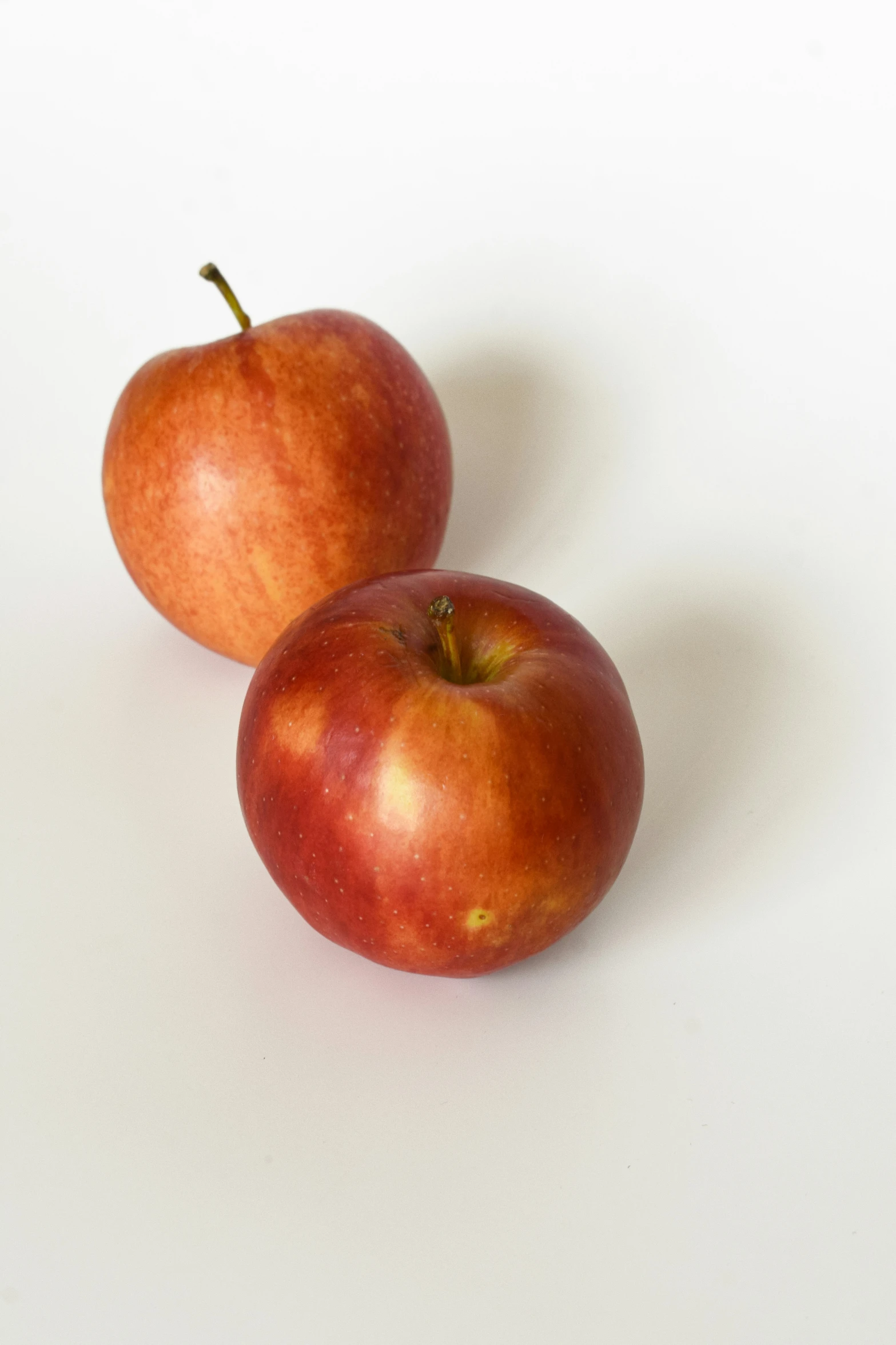 two red apples sitting on top of a white surface