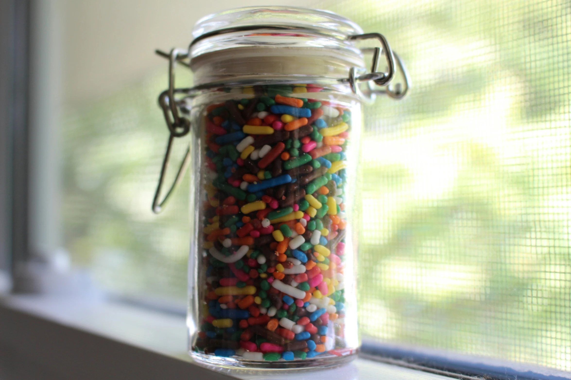 sprinkles and cookies in a glass jar sitting on a window sill